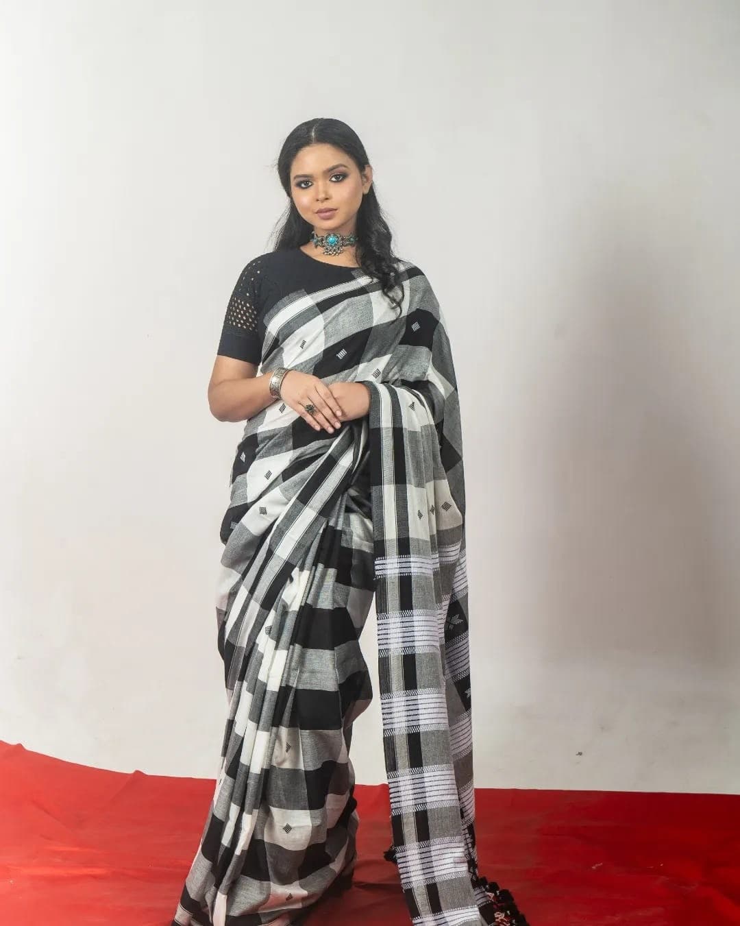 Sanjana Murmu standing straight in a black and white checked saree, pallu gathered at her shoulder.
