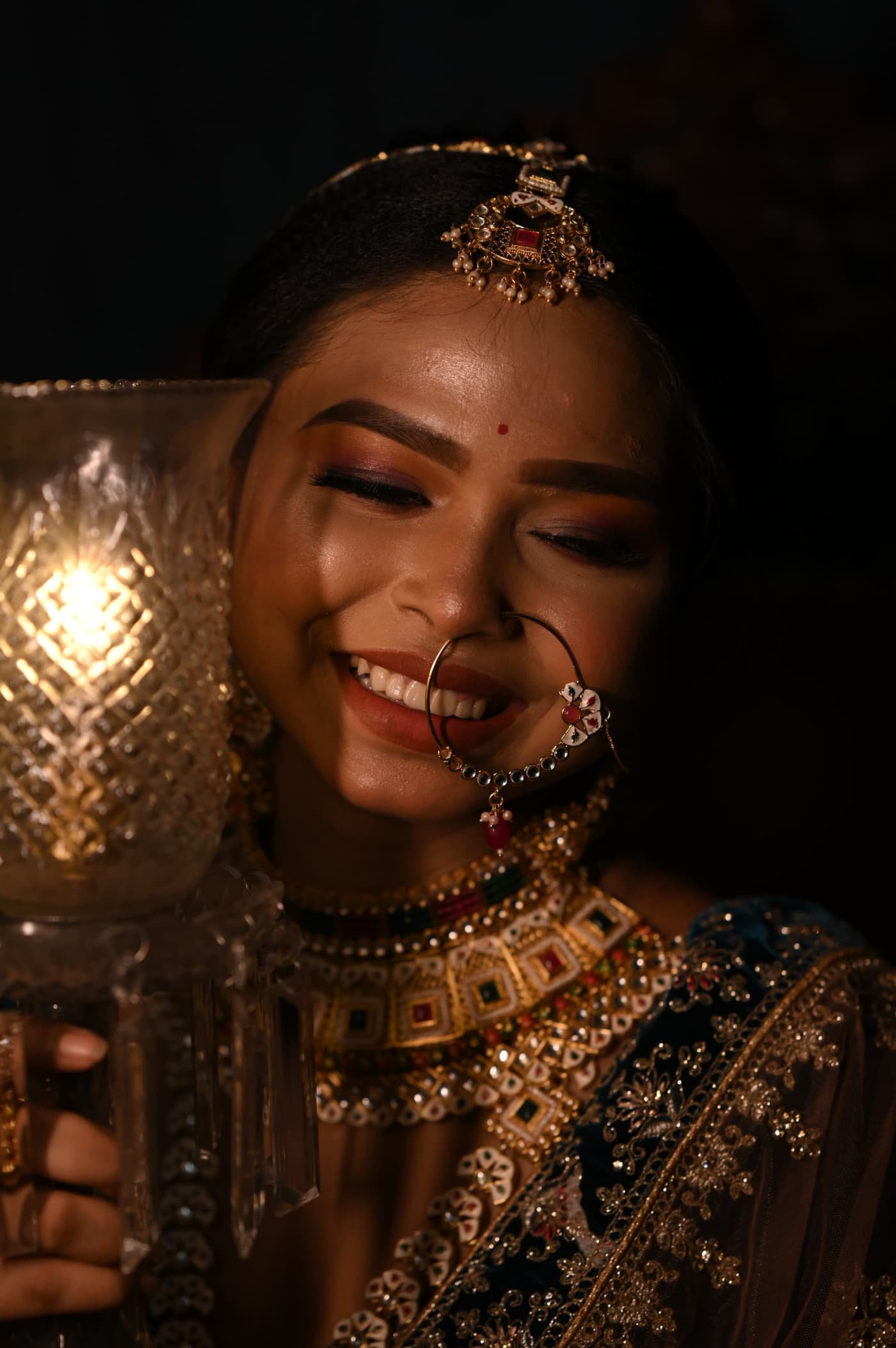 Sanjana Murmu lit by the glow of a lantern she holds, laughing, wearing a gold kundan choker and nose ring.